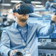 A man wearing a VR headset works inside an office using motion-tracking controllers.